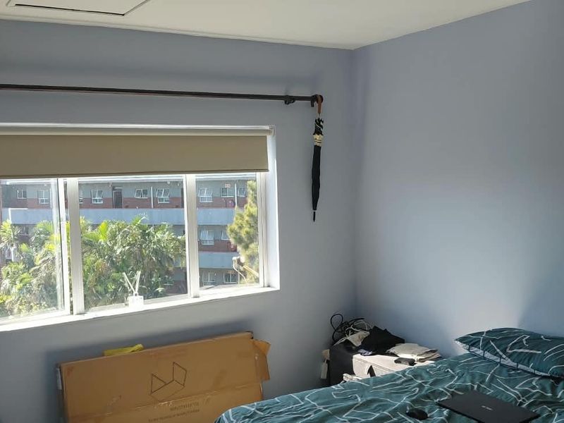 A bedroom featuring a split-system air conditioner, a window with a roller blind, and a curtain rod.