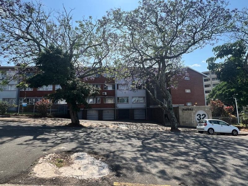 Street view of the front facade of the Pafuri apartment complex, featuring brick exterior, secure garage access, and mature trees.