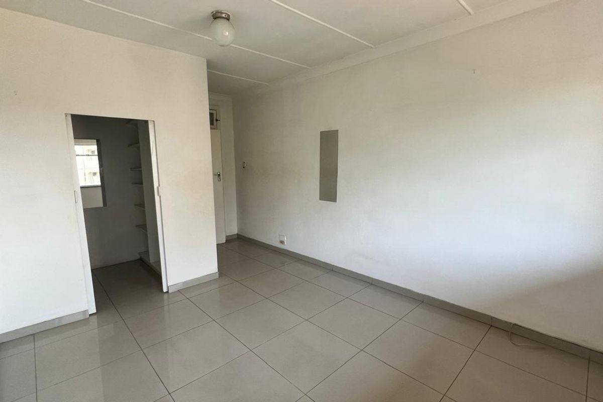 An empty living area featuring neutral tiled flooring and a small walk-in storage space with built-in shelving.