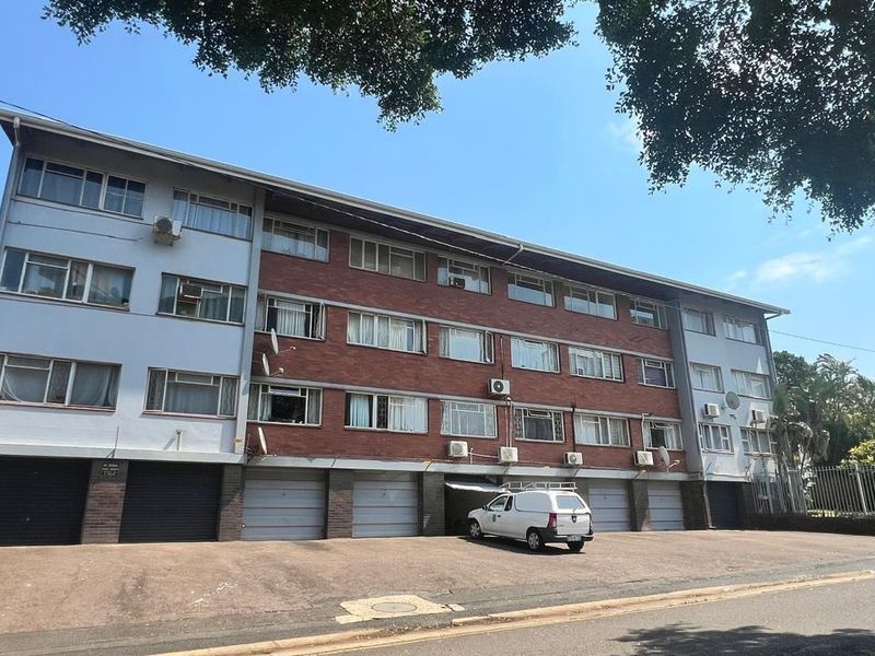 Front elevation of a multi-story apartment building featuring brick and painted facade, ground-level garage access, and exterior air conditioning units.
