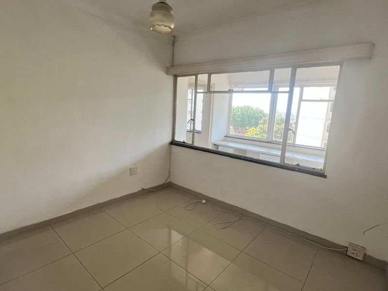 An empty bedroom featuring tiled flooring, a large metal-framed window, and neutral walls, offering a blank canvas for renovation or interior design.