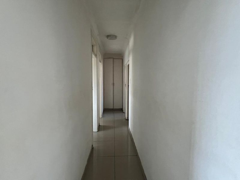 A clean, empty hallway featuring tiled flooring and a built-in storage cupboard at the end.