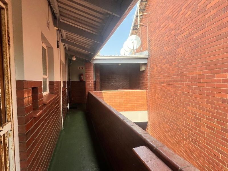 An exterior apartment building walkway featuring brick walls, a corrugated metal roof, and a security gate entrance.