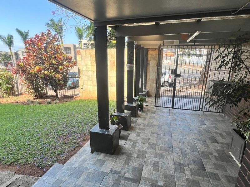 A covered patio area featuring tiled flooring, support pillars, and a secure metal gate leading to the garden.