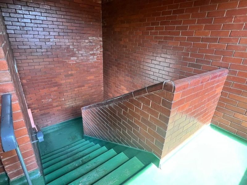 A functional stairwell featuring exposed brick walls and painted concrete steps with a fixed handrail, providing access between levels in the apartment building.