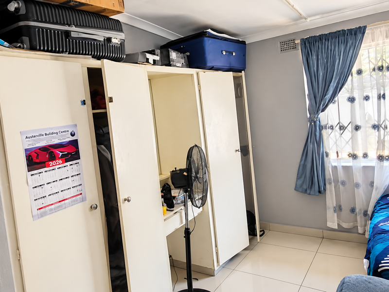 A functional bedroom featuring built-in cupboards, tiled flooring, and a window fitted with security gates and curtains.