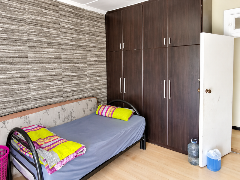 A bedroom featuring dark wood built-in cupboards, laminate flooring, and a textured feature wall, with an adjacent doorway leading to a utility area.