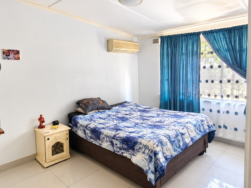 A functional bedroom featuring tiled flooring, an integrated air conditioning unit, and a window fitted with a security gate.