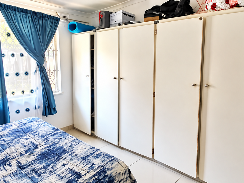 A bedroom featuring extensive built-in cupboards, tiled flooring, and a window with security bars, offering functional storage space.