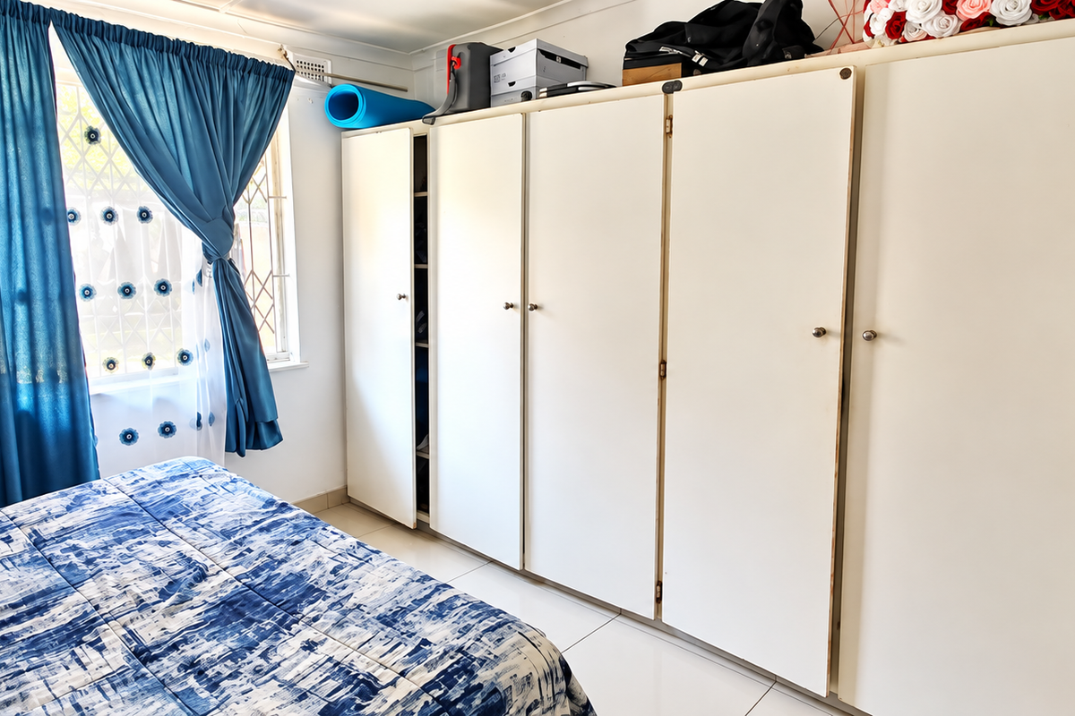 A bedroom featuring extensive built-in cupboards, tiled flooring, and a window with security bars, offering functional storage space.