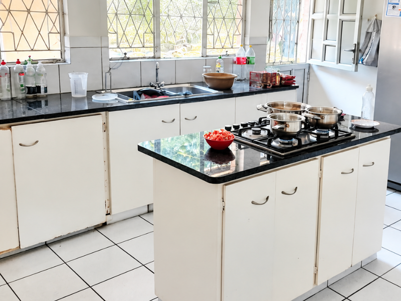 Functional kitchen featuring white cabinetry, granite countertops, a central island with a built-in gas hob, and tiled flooring throughout.