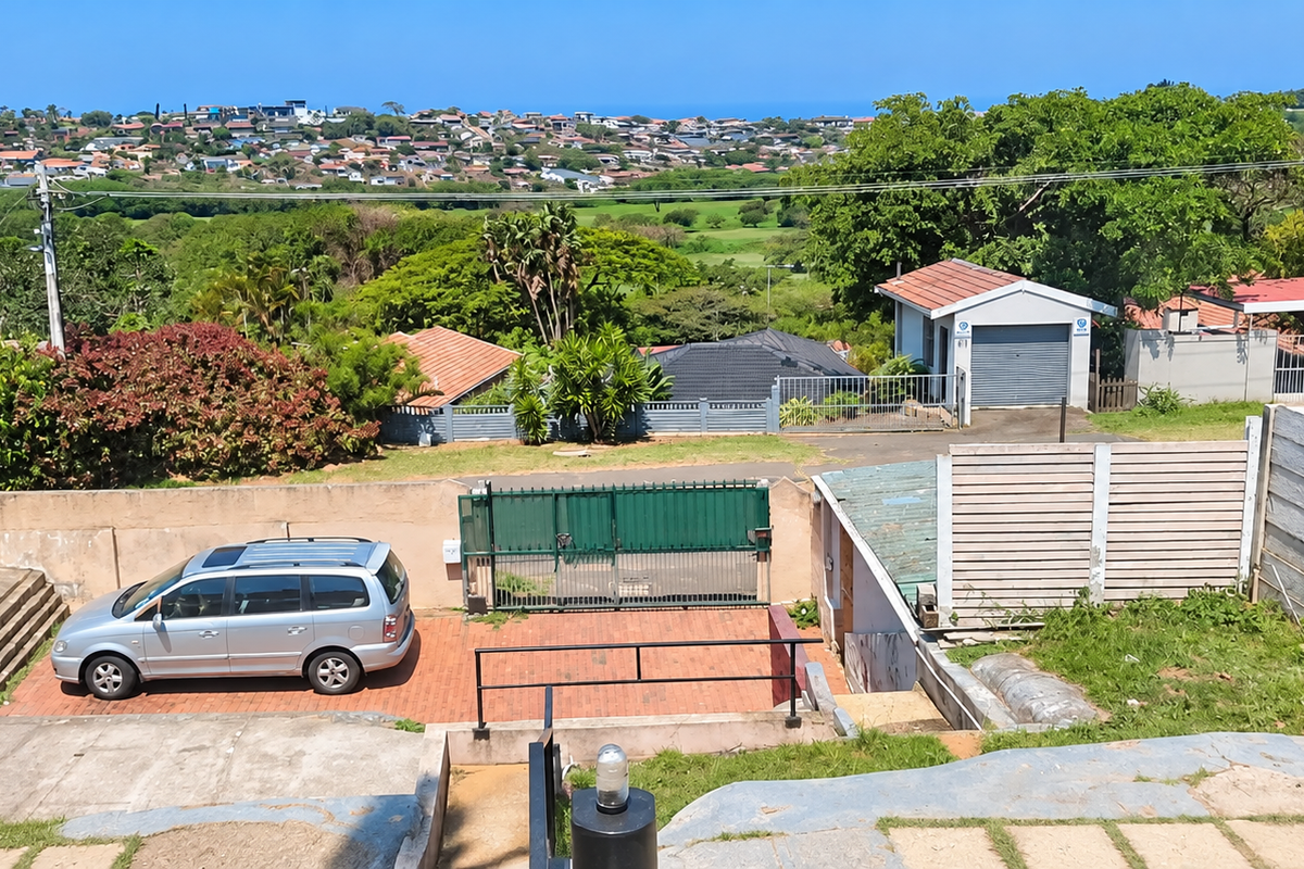 Rear exterior view featuring a paved driveway, secure gated access, detached garage, and expansive neighbourhood views.