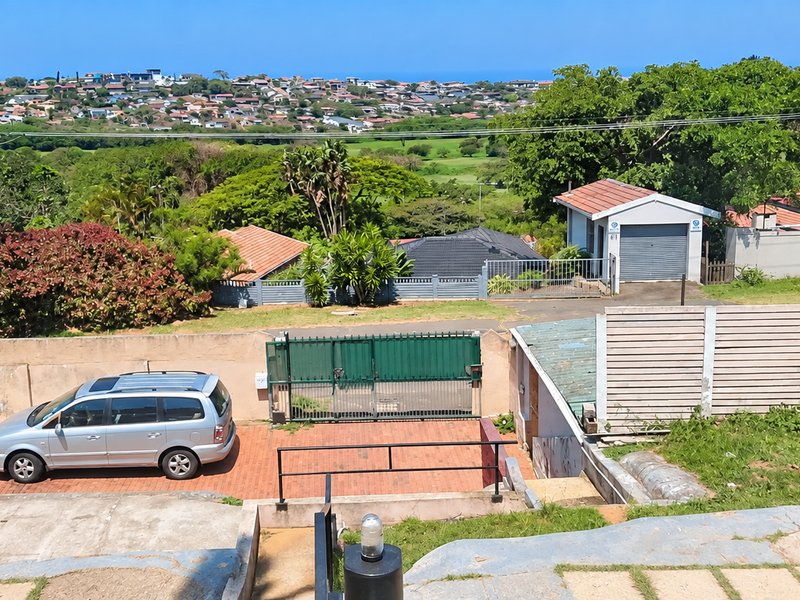 Rear exterior view featuring a paved driveway, secure gated access, detached garage, and expansive neighbourhood views.