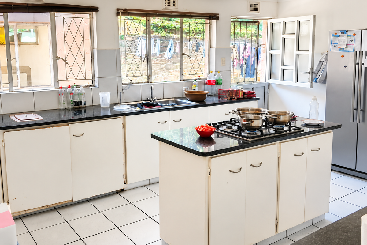 Spacious kitchen featuring granite countertops, a central island with a gas hob, tiled flooring, and ample built-in cabinetry with security-barred windows.