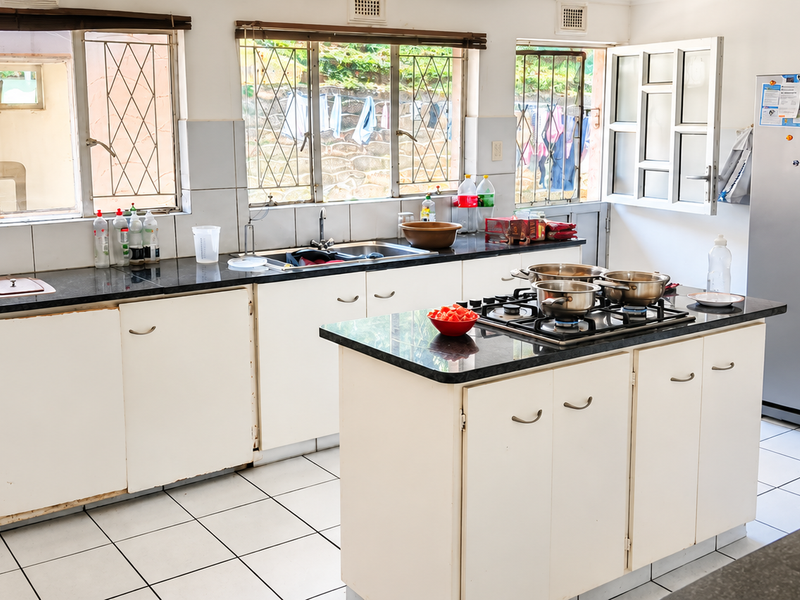 Spacious kitchen featuring granite countertops, a central island with a gas hob, tiled flooring, and ample built-in cabinetry with security-barred windows.