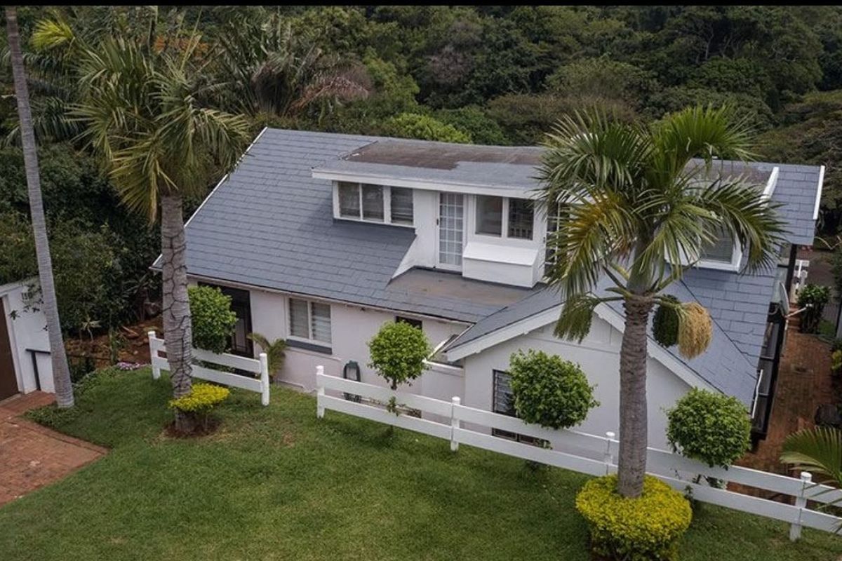 Aerial view of a residential property featuring a slate roof, dormer windows, and a well-maintained garden with a white picket fence.