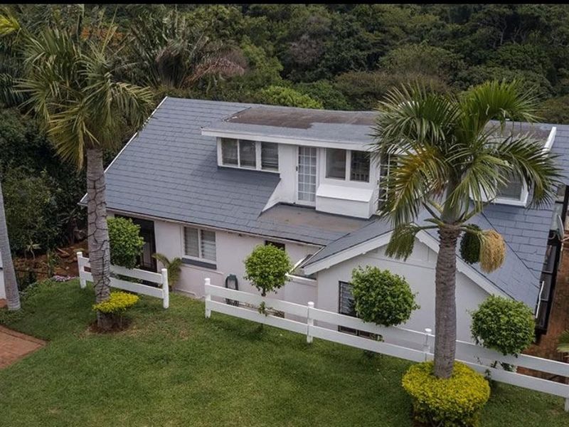 Aerial view of a residential property featuring a slate roof, dormer windows, and a well-maintained garden with a white picket fence.