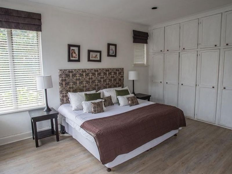 Spacious bedroom featuring light-toned laminate flooring, extensive built-in cabinetry, and large windows with fitted venetian blinds.