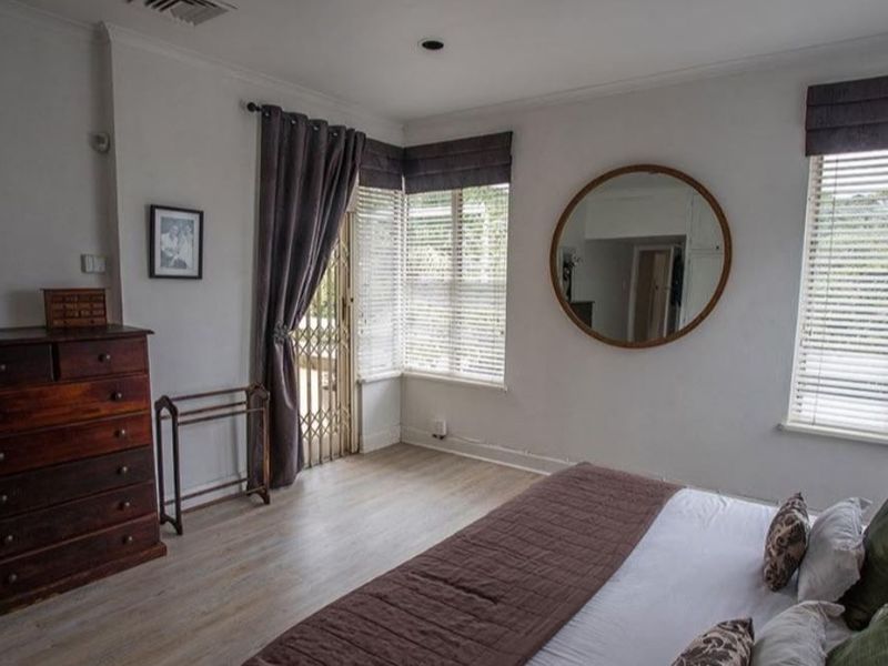 A well-lit bedroom featuring laminate flooring, recessed downlights, and large windows with venetian blinds, providing a comfortable and functional living space.
