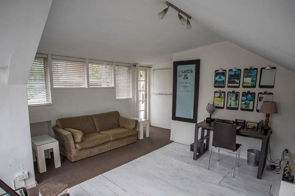 A multi-purpose living area featuring a sloped ceiling, track lighting, and large windows with venetian blinds, offering a versatile space for relaxation or work.