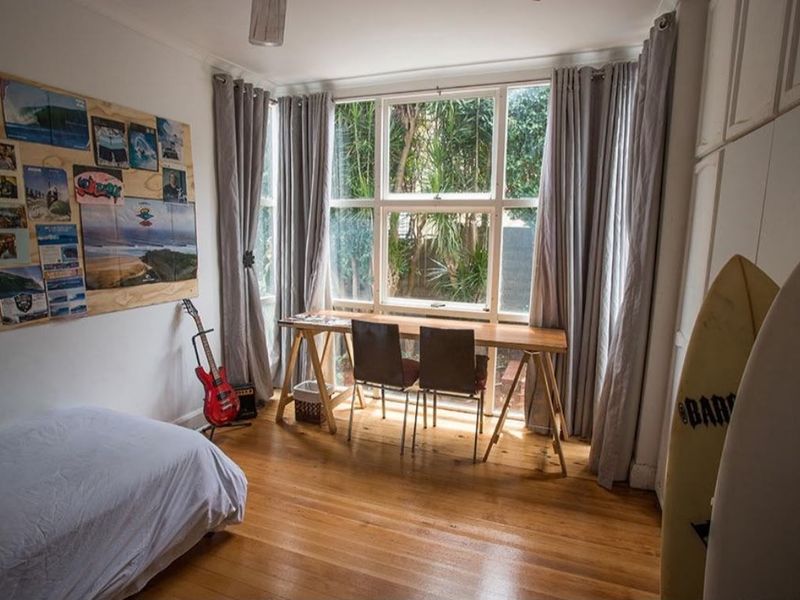 A bedroom featuring polished hardwood flooring, built-in storage cupboards, and a large window providing natural light and garden views.