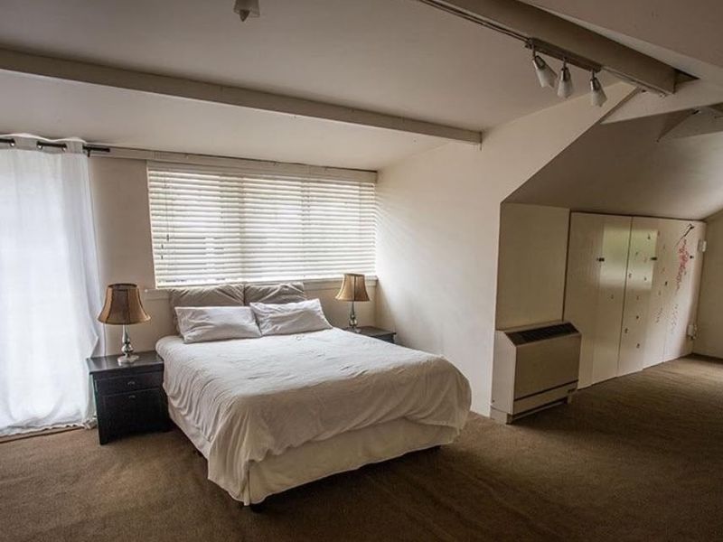 Spacious attic-style bedroom featuring built-in cupboards, sloped ceilings, and track lighting, offering a functional layout with potential for modern updates.
