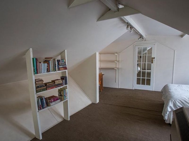 Attic bedroom featuring sloped ceilings, exposed rafters, built-in shelving, and a glass panel door, offering a cozy space with potential for modernization.