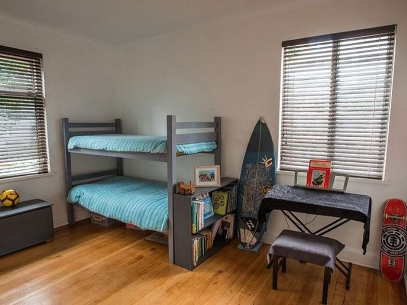 A bedroom featuring polished timber flooring and dual windows fitted with venetian blinds, offering a bright and functional living space.