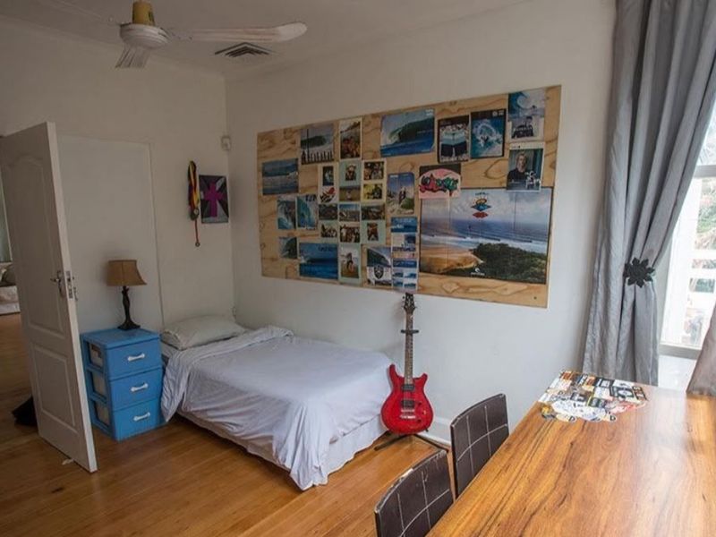 A bedroom featuring timber flooring, a ceiling fan, and ducted air conditioning, offering a functional space with natural light.
