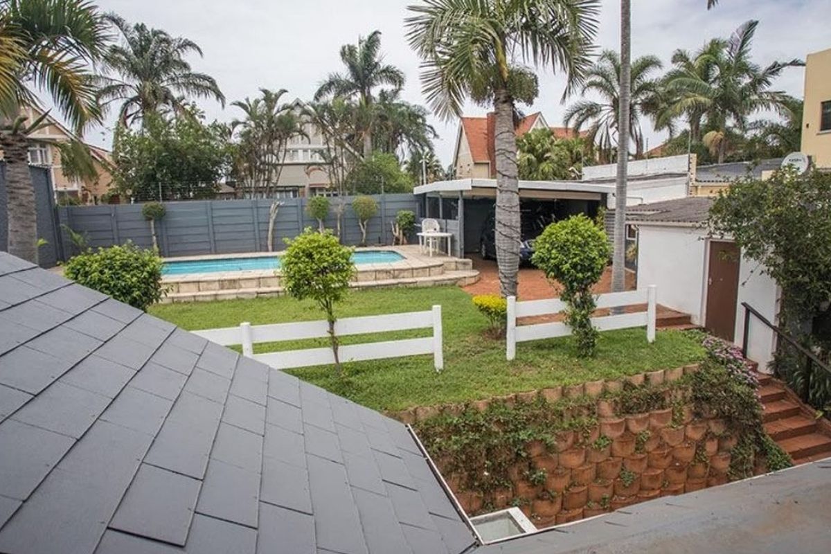Rear view of the property featuring a swimming pool, landscaped garden, retaining wall, and a covered carport area.