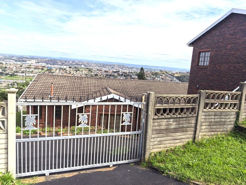 Front exterior view of a brick house featuring a metal sliding gate, precast boundary wall, and an elevated outlook over the surrounding urban area.