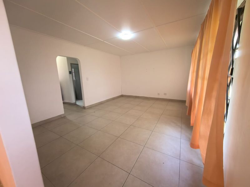 A spacious, empty living room featuring neutral tiled flooring, a simple ceiling finish, and an arched doorway leading to an adjacent area.