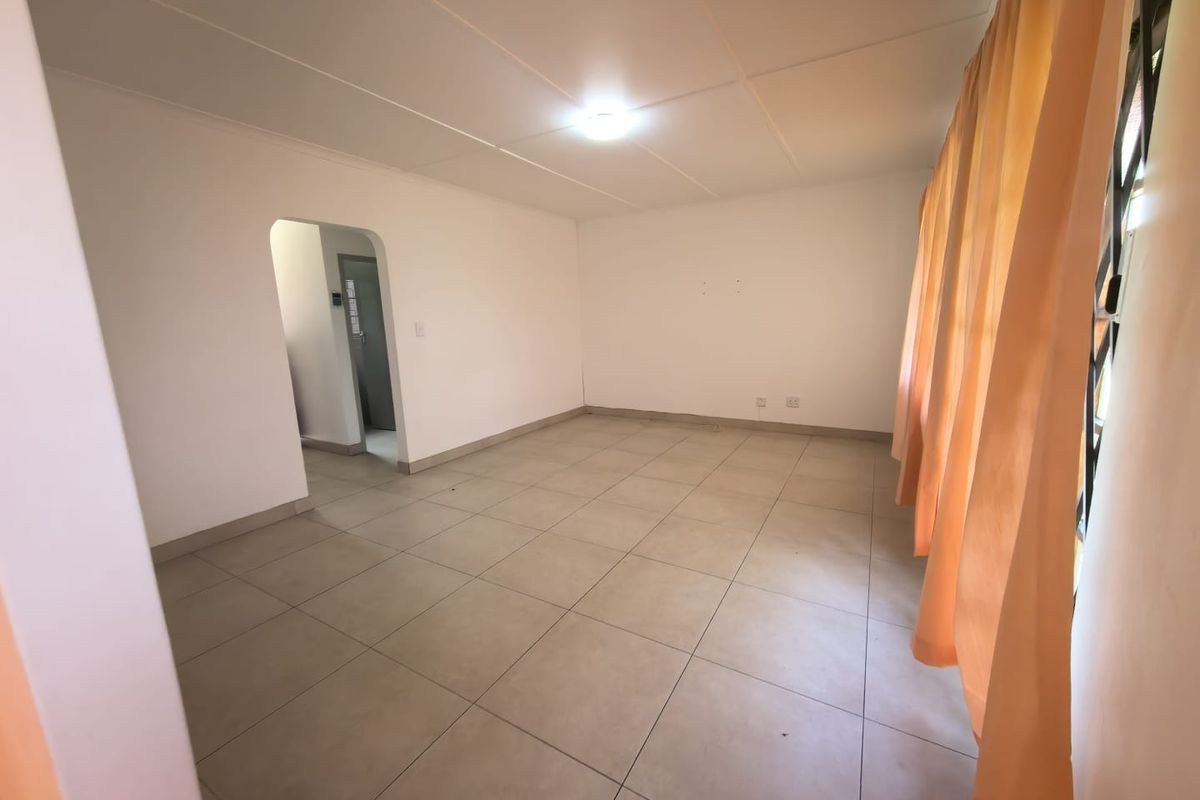 A spacious, empty living room featuring neutral tiled flooring, a simple ceiling finish, and an arched doorway leading to an adjacent area.
