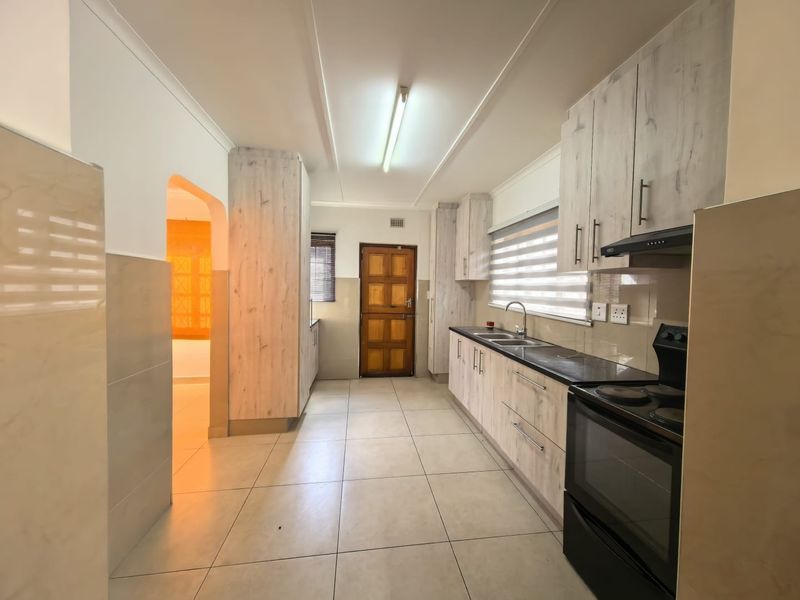 A functional kitchen featuring light wood-grain cabinetry, dark countertops, tiled flooring, and a built-in electric stove with an extractor fan.