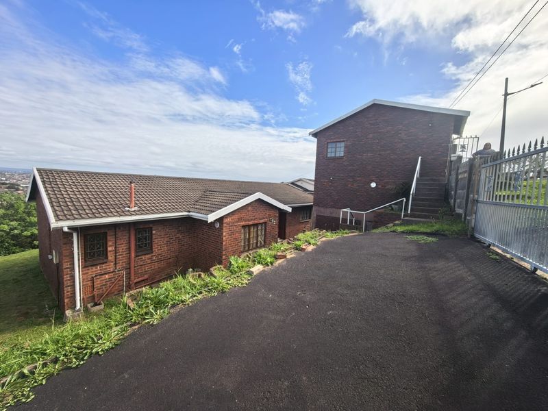 Front exterior view of a brick house featuring a tiled roof, asphalt driveway, and secure metal gate access with external stairs.