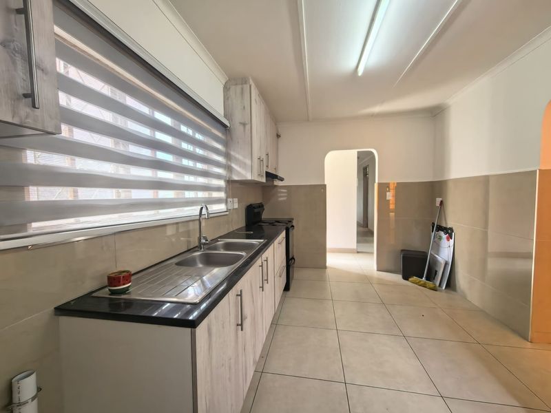 A clean, functional kitchen featuring light wood-look cabinetry, dark countertops, tiled splashbacks, and neutral floor tiles, offering a bright and well-maintained workspace.