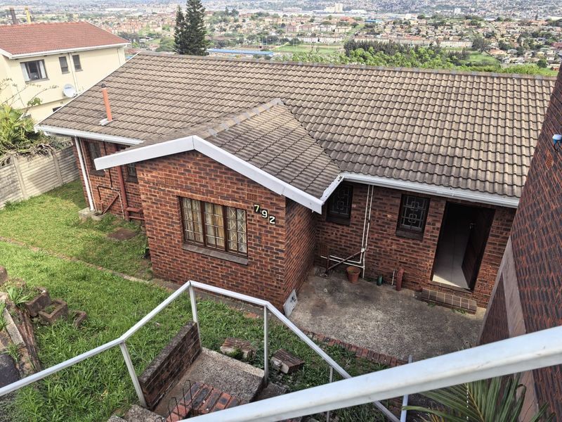 Elevated rear view of a brick house featuring a tiled roof, concrete patio area, and security bars on windows, overlooking a suburban landscape.
