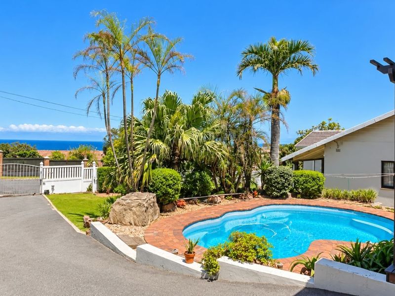 Outdoor pool area featuring a swimming pool with brick coping, a pergola, and a paved driveway, set against a scenic coastal backdrop.