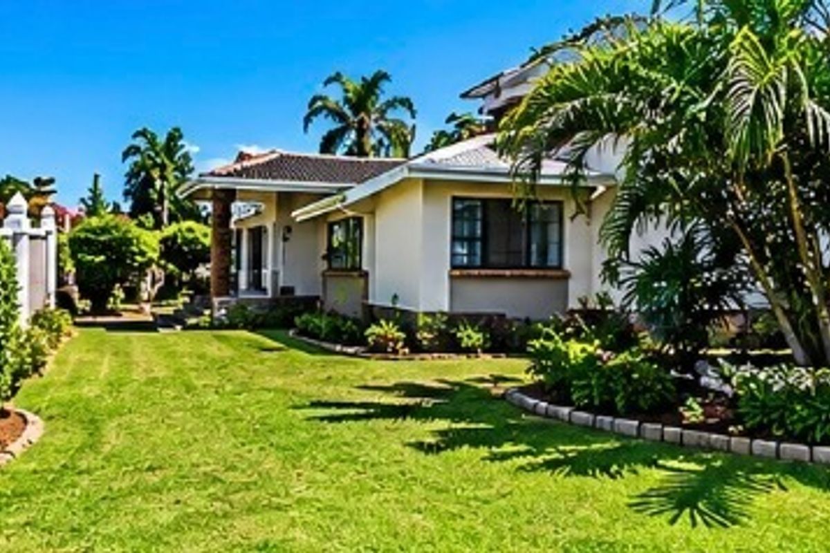 A well-maintained rear garden featuring a lush lawn, mature palm trees, and a tiled roof house exterior with a white picket fence.