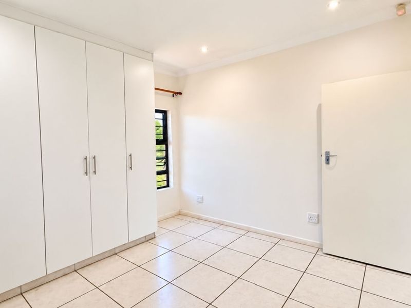 A bright, empty bedroom featuring neutral tiled flooring, ample built-in cupboard storage, and recessed ceiling lighting.