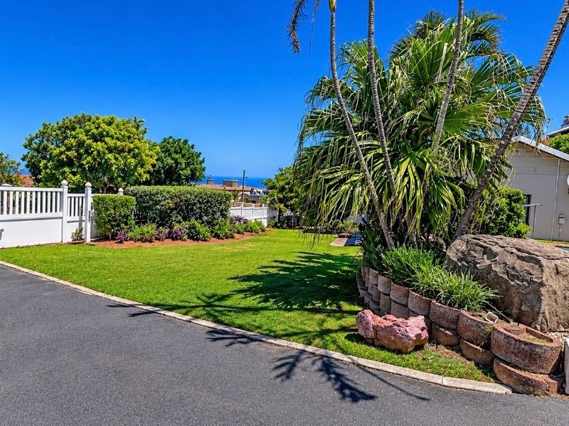 A well-maintained garden area featuring a lush lawn, landscaped retaining wall, asphalt driveway, and a swimming pool, offering a pleasant outdoor space.