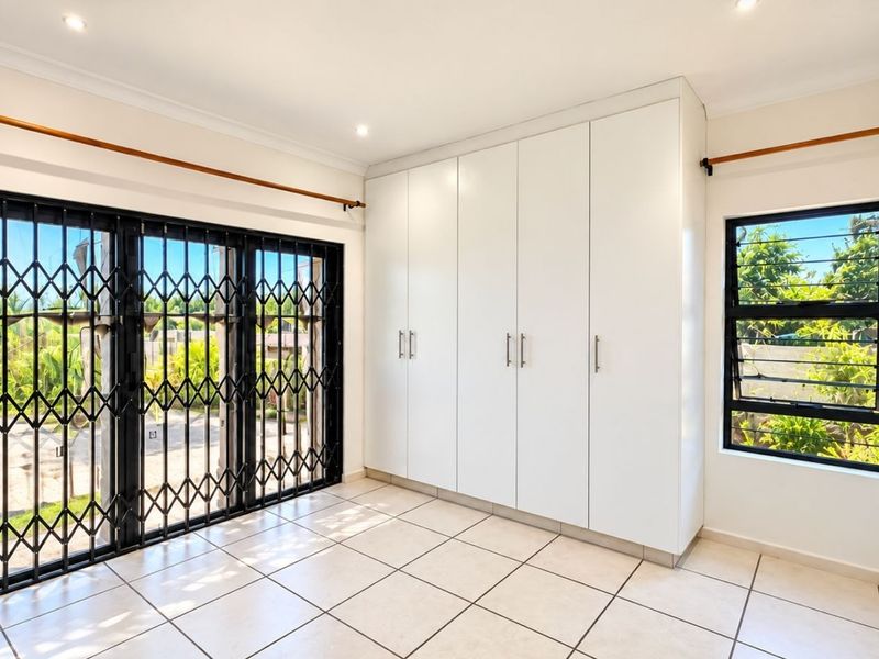 A bright, empty bedroom featuring white built-in cupboards, tiled flooring, and a large sliding door with a security gate leading to the exterior.
