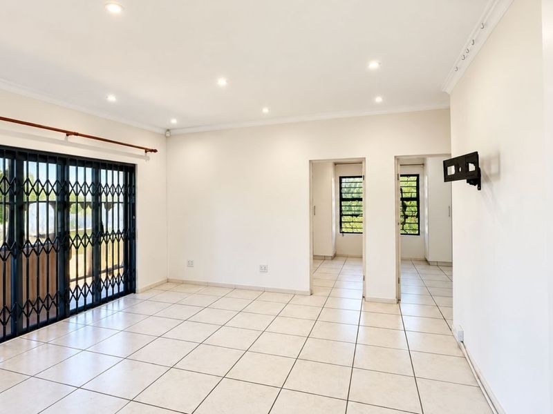 A bright, open-plan living area featuring neutral tiled flooring, recessed lighting, and a secure sliding door leading to the exterior.