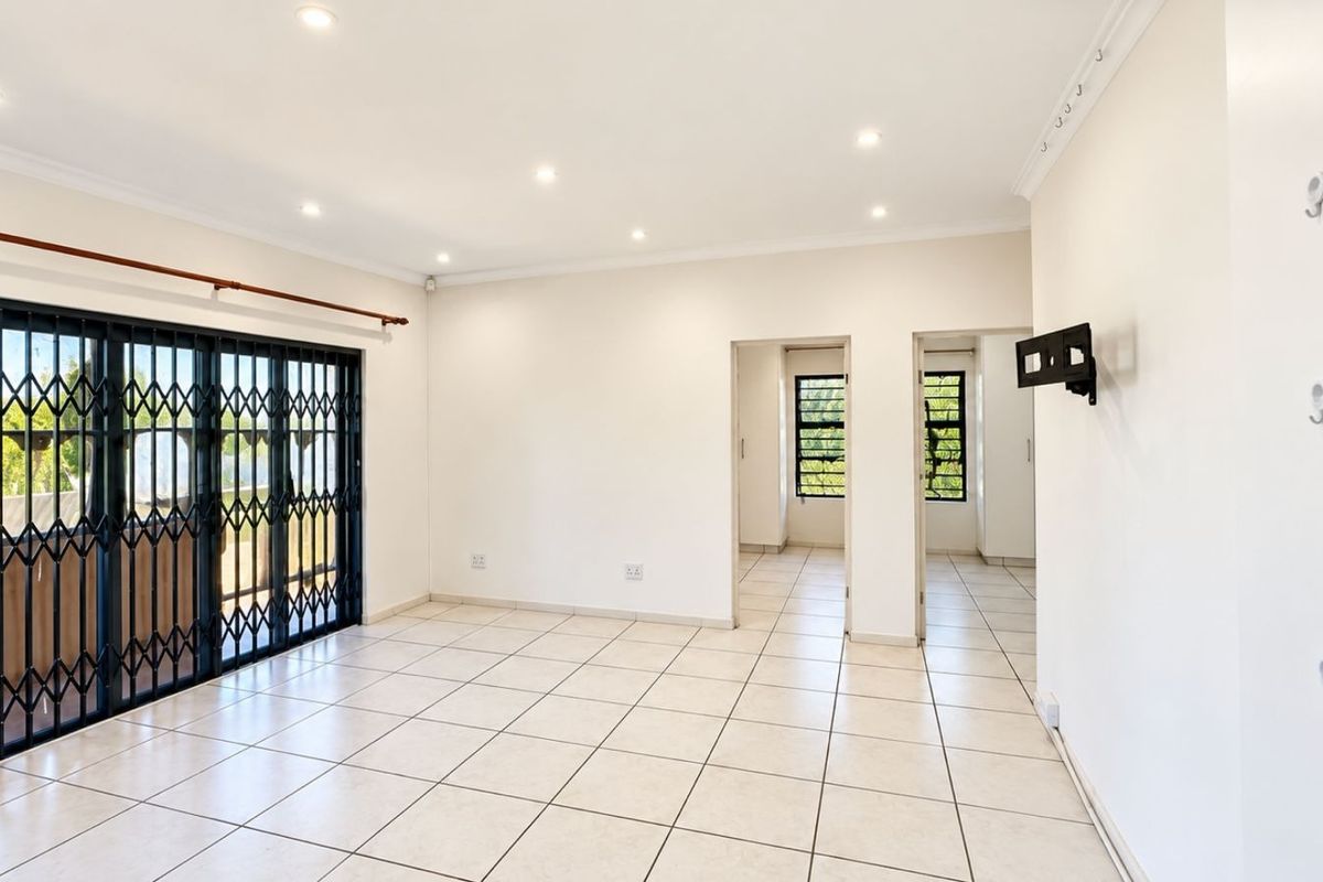 A bright, open-plan living area featuring neutral tiled flooring, recessed lighting, and a secure sliding door leading to the exterior.
