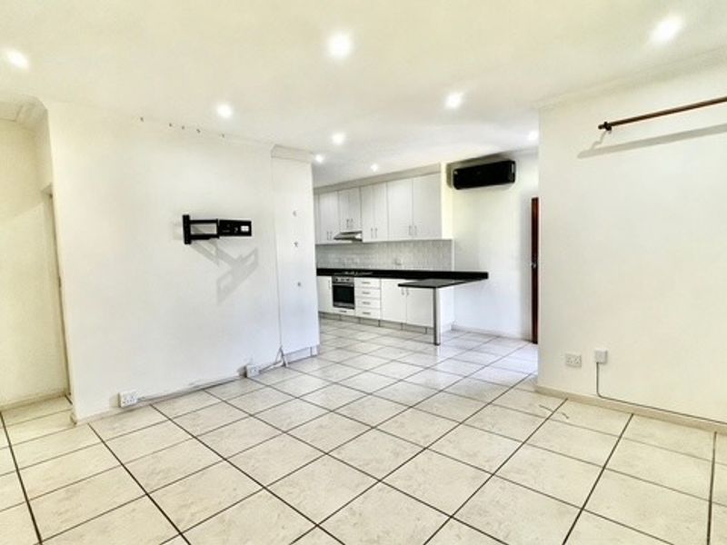 An open-plan living and kitchen area featuring tiled flooring, recessed lighting, and a functional kitchen with built-in cabinetry and appliances.