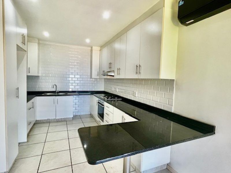 Modern kitchen featuring white cabinetry, subway tile backsplash, dark granite countertops, built-in oven, gas hob, and a breakfast bar peninsula.
