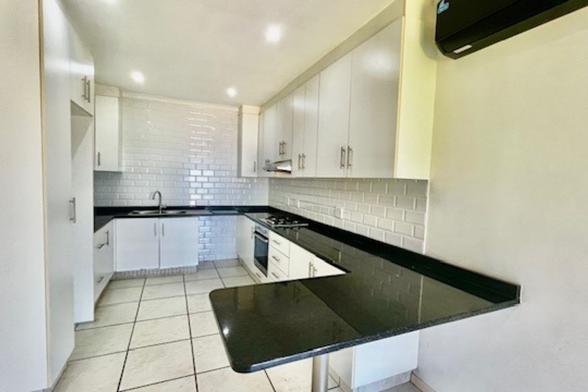 Modern kitchen featuring white cabinetry, subway tile backsplash, dark granite countertops, built-in oven, gas hob, and a breakfast bar peninsula.