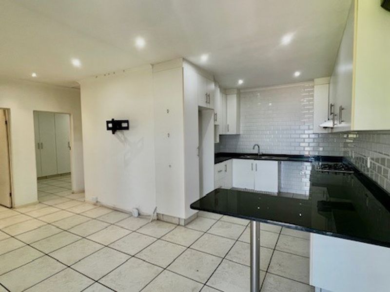 Open plan kitchen and living area featuring white cabinetry, black granite countertops, subway tile backsplash, and neutral ceramic floor tiles throughout.