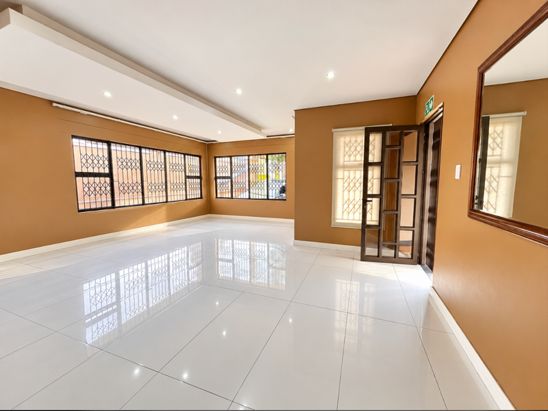 A spacious, empty living area featuring polished white floor tiles, recessed ceiling lighting, and secure window treatments.