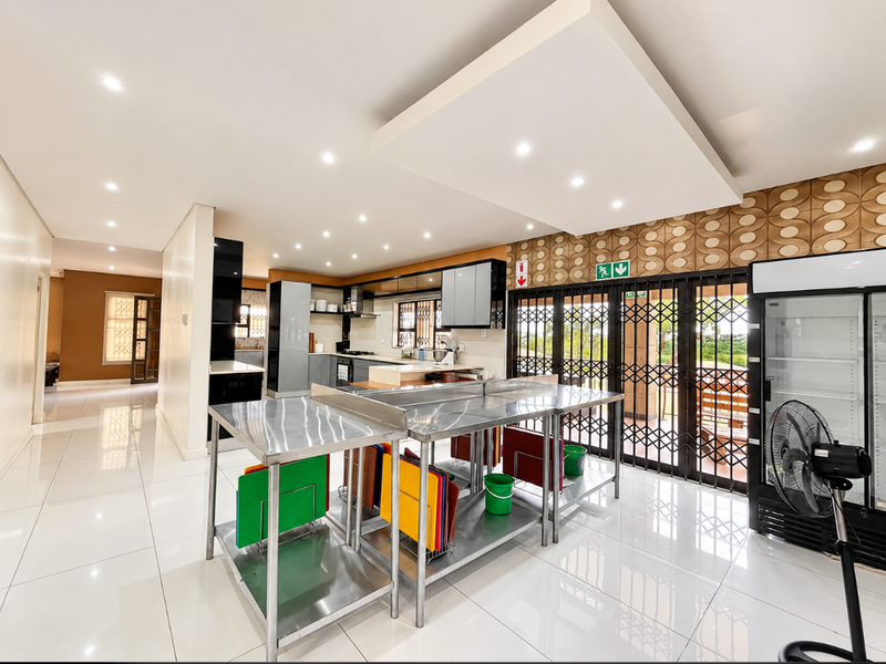 Spacious kitchen area featuring modern tiled flooring, recessed ceiling lighting, and stainless steel prep stations, with direct access to an outdoor area via security gates.